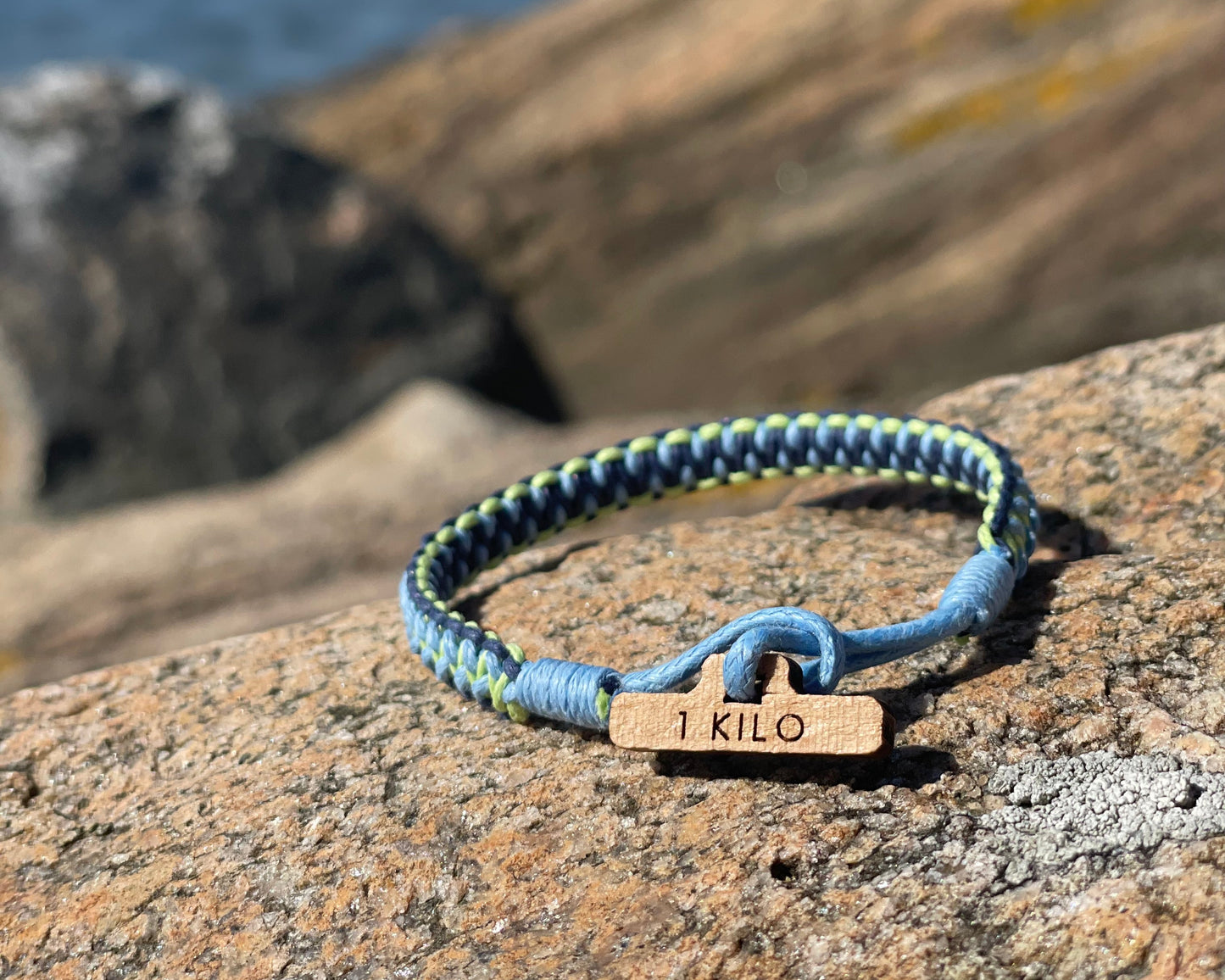 CleanSea bracelet with a wooden tag on a rocky surface.