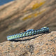 CleanSea bracelet on a rock, with rocks in background. Bracelet is dark blue, light blue and light green to symbolise land and sea. 