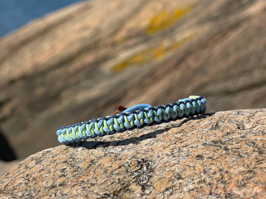 CleanSea bracelet on a rock, with rocks in background. Bracelet is dark blue, light blue and light green to symbolise land and sea. 